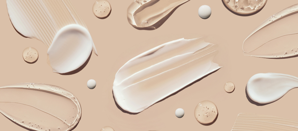 Various textures and shades of skincare or cosmetic creams and gels are spread out on a light beige background, reminiscent of the expert care provided by West Michigan Dermatology.