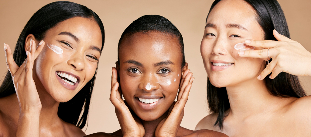 Three individuals smiling, applying skincare cream to their faces against a beige background, reflect the essence of care and expertise found at West Michigan Dermatology.