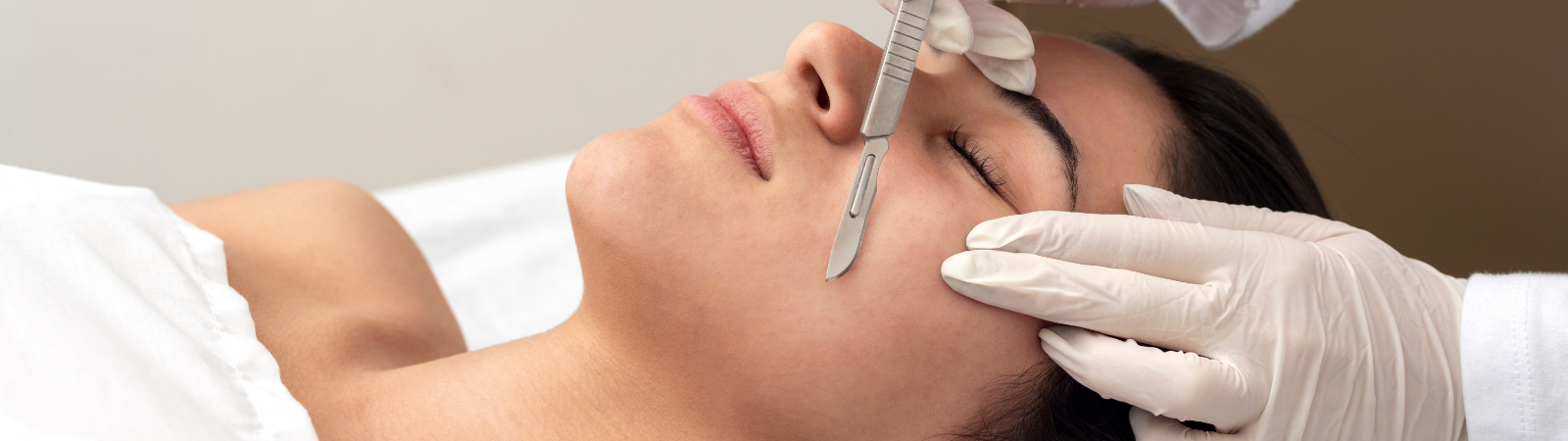 A person undergoing a facial procedure with a scalpel, performed by a professional wearing white gloves.