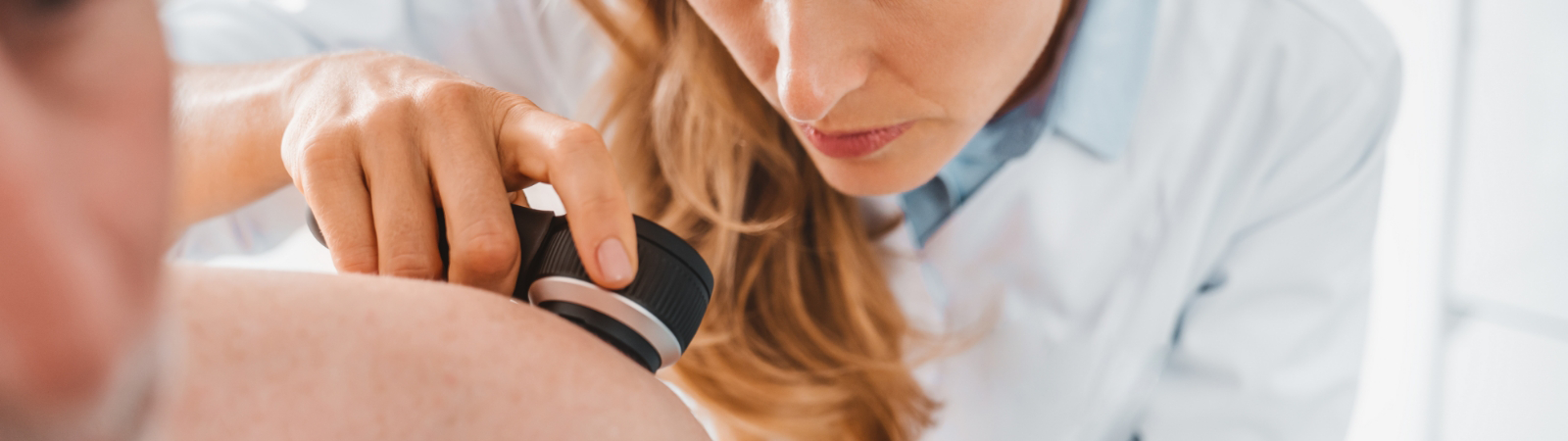 A medical professional closely examines a patient's skin using a dermatoscope.